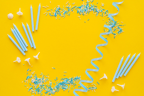 Top view of candles near blue serpentine and sprinkles on yellow background