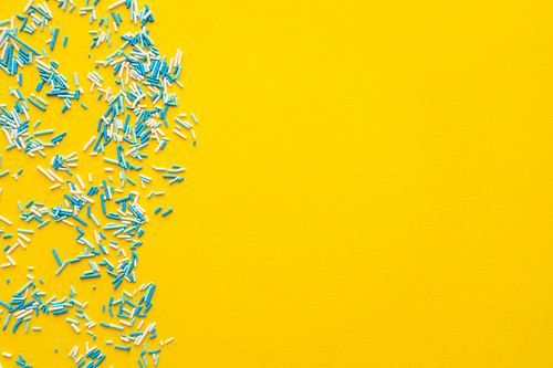 Top view of blue and white sweet sprinkles on yellow background