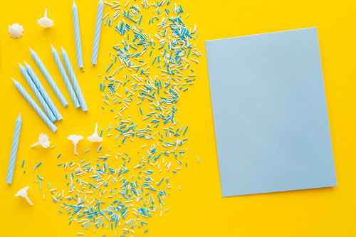 Top view of empty blue greeting card near sprinkles and candles on yellow background