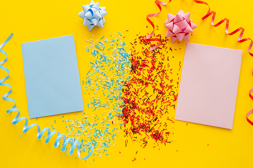 Top view of blue and pink greeting cards near sprinkles and serpentine on yellow background