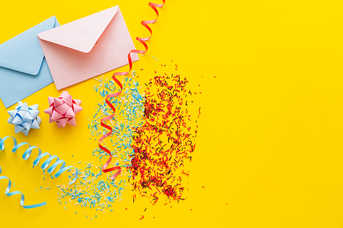 Top view of blue and pink envelopes near serpentine and sprinkles on yellow background