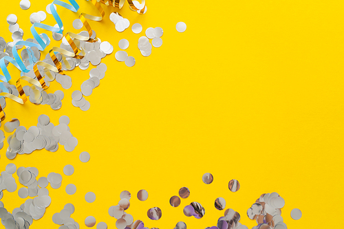 Top view of colorful serpentine and confetti on yellow background