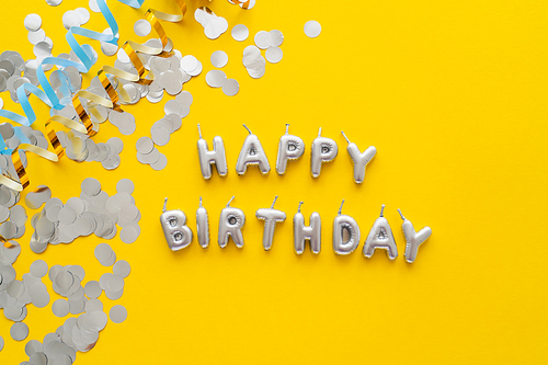 Top view of candles in shape of Happy Birthday lettering and confetti on yellow background