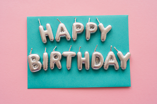 Top view of candles in shape of Happy Birthday lettering on card on pink background