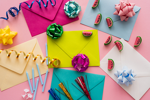 Top view of colorful envelopes near candies and serpentine on pink background