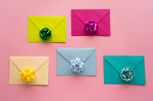 Top view of colorful gift bows on envelopes on pink background