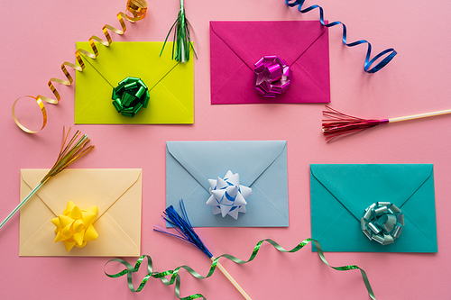 Top view of colorful gift bows on envelopes near serpentine on pink background