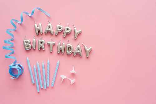 Top view of candles in shape of Happy Birthday lettering near blue serpentine on pink background