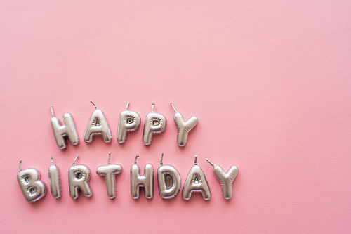 Top view of silver candles in shape of Happy Birthday lettering on pink background
