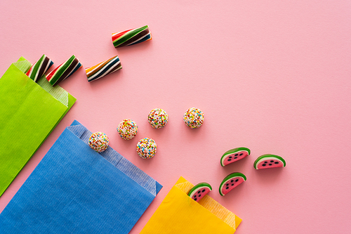 Top view of sweet candies and paper bags on pink background
