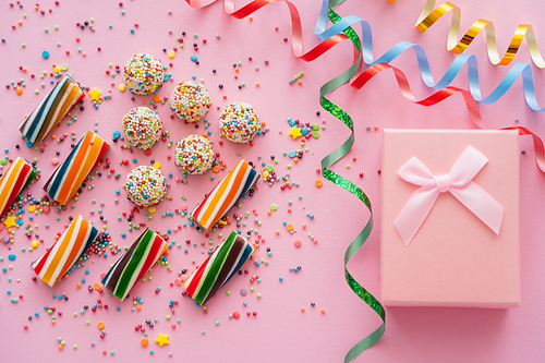 Top view of gift box near serpentine and colorful candies on pink background