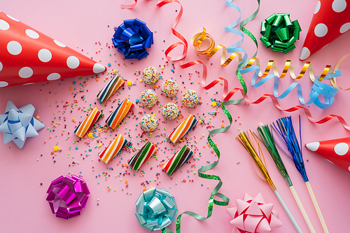 Top view of colorful sweets near serpentine and party caps on pink background