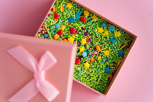 Top view of colorful sprinkles in gift box on pink background