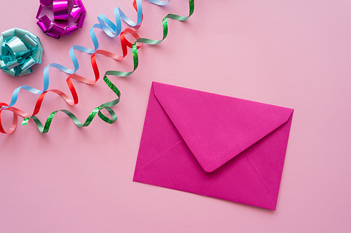 Top view of envelope near serpentine and gift bows on pink background