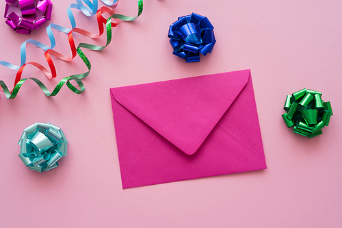Top view of envelope near gift bows and serpentine on pink background