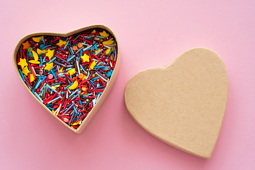 Top view of colorful sprinkles in heart shaped box on pink background