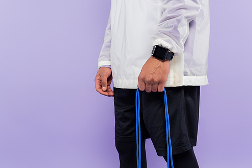 cropped view of african american man with smart watch holding skipping rope isolated on purple