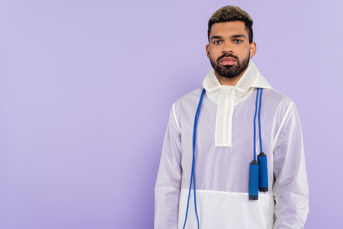 young african american man in trendy sportswear with skipping rope isolated on purple