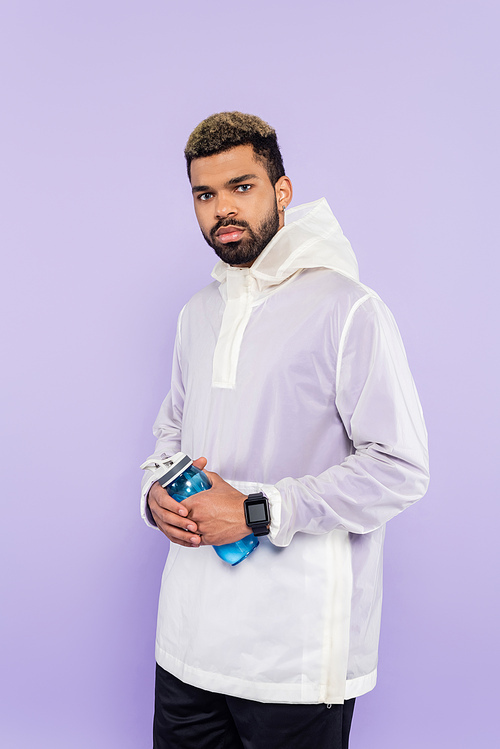 african american man in trendy sportswear holding sports bottle isolated on purple