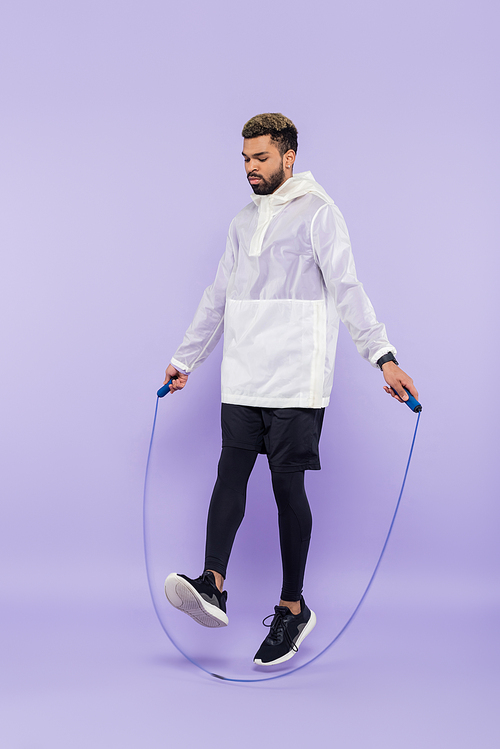 full length of african american sportsman in sportswear exercising with skipping rope on purple