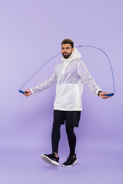 full length of young african american sportsman in sportswear exercising with skipping rope on purple