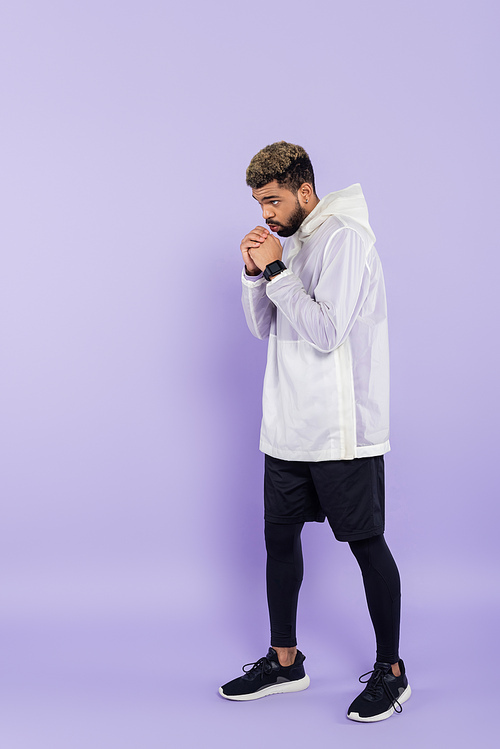 full length of bearded african american man in sportswear warming up on purple