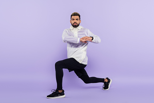 full length of bearded african american sportsman in sportswear warming up on purple