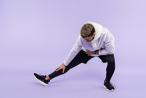 full length of african american sportsman in sportswear doing lunges on purple