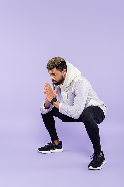 full length of bearded african american sportsman in sportswear working out with praying hands on purple