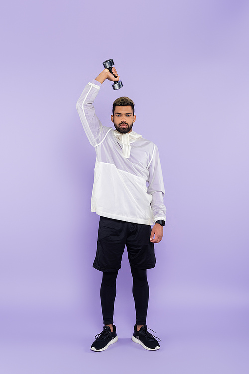 full length of bearded african american man exercising with dumbbell on purple