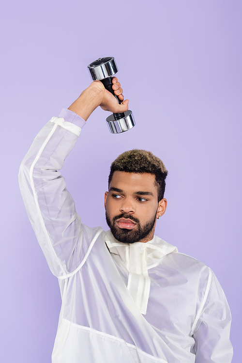 bearded african american man working out with dumbbell isolated on purple