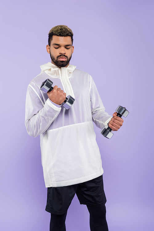 bearded african american sportsman exercising with dumbbells isolated on purple