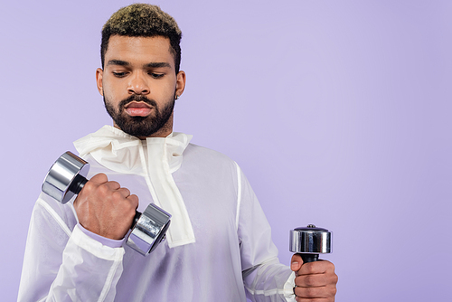 strong african american sportsman exercising with dumbbells isolated on purple