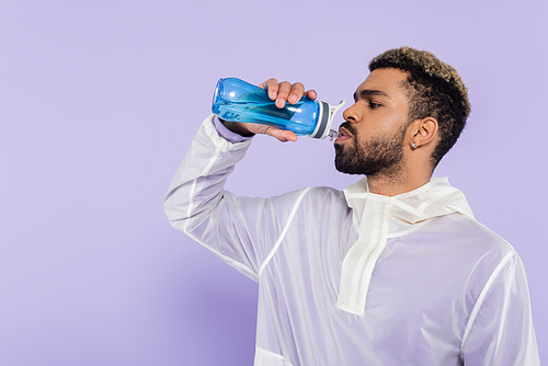 bearded african american sportsman holding sports bottle and drinking refreshing water on purple