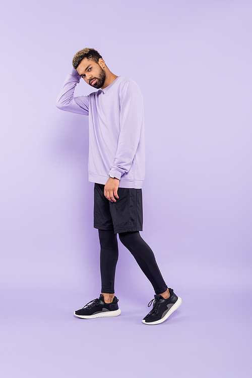 full length of bearded african american man in sweater and shorts standing on purple