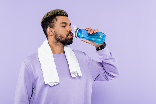 young african american man in sweater standing with white towel and drinking water isolated on purple