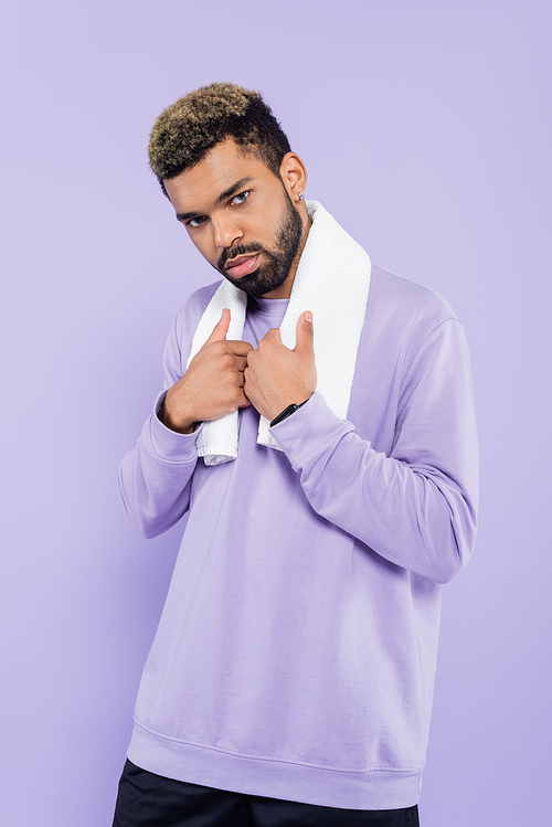 bearded african american man in sweater holding white towel and looking at camera isolated on purple