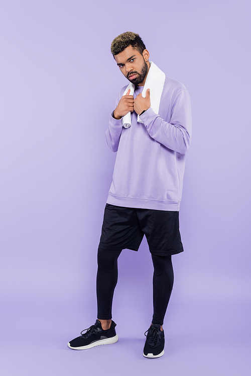 full length of bearded african american man in sweater holding white towel and looking at camera on purple