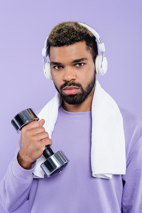 bearded african american man in headphones exercising with dumbbell isolated on purple