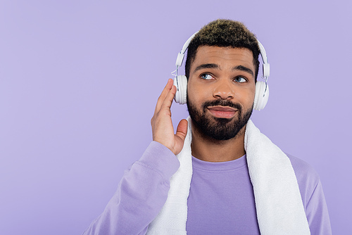 pleased and bearded african american man in wireless headphones isolated on purple