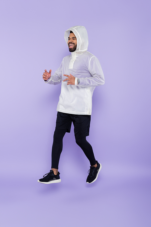 full length of cheerful african american man in sportswear levitating on purple