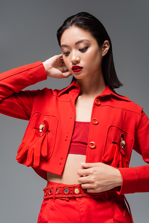 young asian model in red blazer decorated with brooches and gloves isolated on grey
