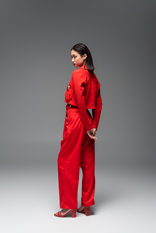 full length of asian woman in red blazer and pants standing on grey background