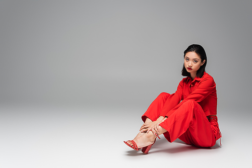 young asian woman looking at camera while sitting in red trendy outfit on grey background