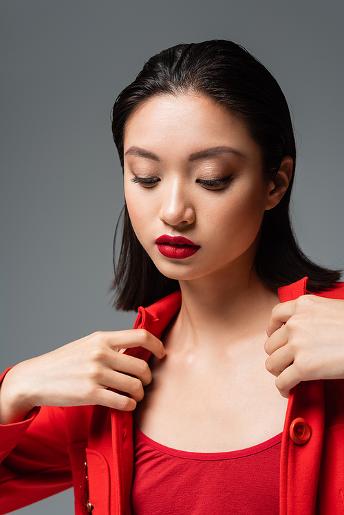 young asian woman with red lips touching stylish jacket isolated on grey