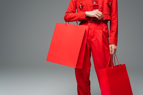 partial view of woman in red suit standing with shopping bags on grey background