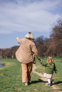 back view of woman pointing with hand while walking with daughter outdoors