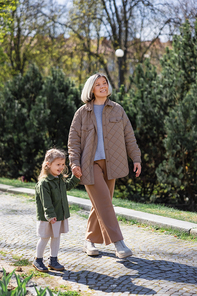 full length of happy and stylish woman with daughter walking in spring park