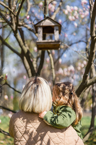 back view of mother and daughter near blurred birdhouse in park