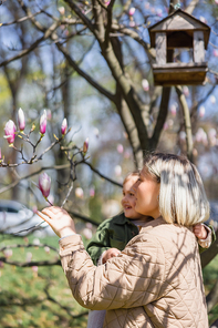 happy mother and daughter looking at blossoming magnolia tree in park